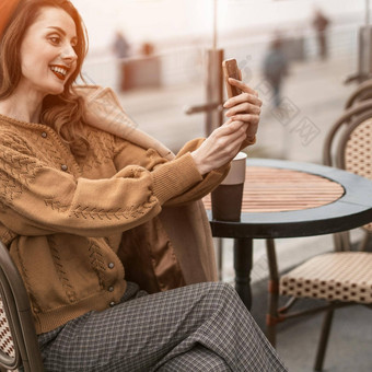 美丽的年轻的女人视频调用智能手机杯咖啡坐着春天户外咖啡馆法国女人红色的贝雷帽背景城市城市广场裁剪
