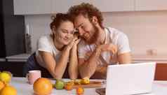 美丽的年轻的夫妇会说话的视频调用移动PC年轻的夫妇烹饪健康的食物厨房首页男人。靠女孩微笑看浪漫的电影