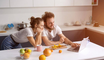 年轻的夫妇烹饪健康的食物厨房首页女孩靠男人。微笑看浪漫的电影美丽的年轻的夫妇会说话的视频调用移动PC