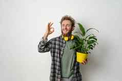 手势持有黄色的花能植物年轻的英俊的有胡子的男人。穿着格子衬衫黄色的耳机脖子孤立的白色背景移动概念