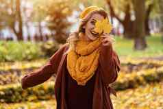 快乐笑女人隐藏眼睛泛黄叶黄色的针织贝雷帽秋天叶子手秋天黄色的花园公园美丽的微笑年轻的女人秋天树叶