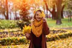 快乐隐藏眼睛女人泛黄叶黄色的针织贝雷帽秋天叶子手秋天黄色的花园公园美丽的微笑年轻的女人秋天树叶