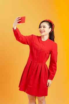 年轻的快乐有吸引力的女红色的衣服需要照片移动电话拍摄色彩斑斓的橙色背景