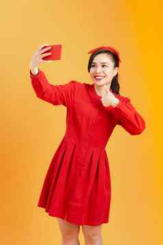 肖像微笑亚洲女人红色的衣服使自拍照片智能手机孤立的橙色背景