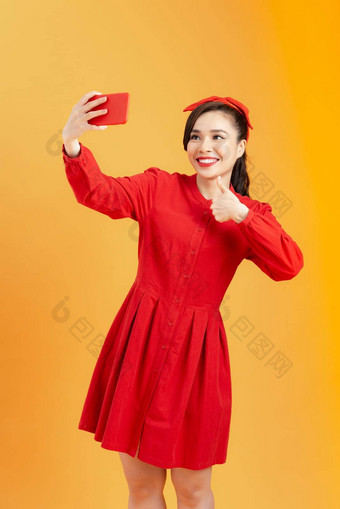 肖像微笑亚洲<strong>女</strong>人红色的衣服使<strong>自拍</strong>照片智能手机孤立的橙色背景