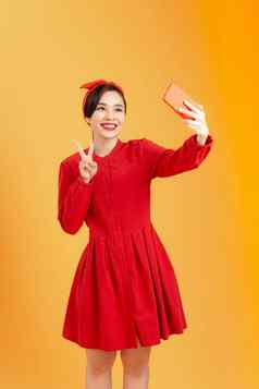 年轻的快乐有吸引力的女红色的衣服需要照片移动电话拍摄色彩斑斓的橙色背景