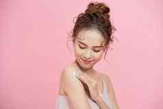 年轻的亚洲女人应用奶油乳液皮肤手臂孤立的粉红色的背景
