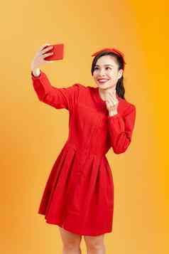 快乐的年轻的亚洲女人红色的衣服采取自拍视频调用站孤立的橙色背景