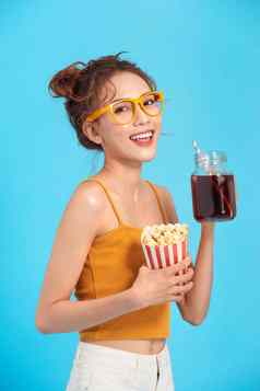 微笑年轻的亚洲女人看电影电影持有桶爆米花杯苏打水