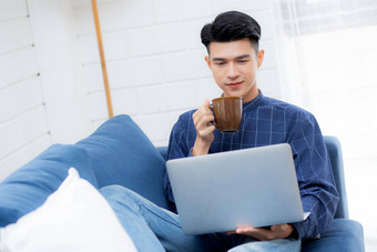 年轻的亚洲商人微笑工作首页移动PC电脑在线沙发生活房间自由业务男人。笔记本喝咖啡沙发上正常的生活方式概念