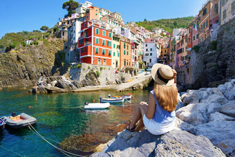 假期意大利漂亮的年轻的女人坐着石头享受城市景观riomaggiore小镇色彩斑斓的房子五渔村意大利
