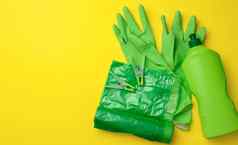 橡胶绿色手套清洁垃圾塑料袋卷塑料瓶洗涤剂黄色的背景
