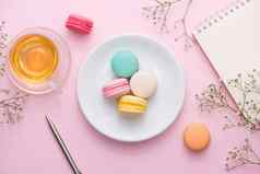 平铺笔记本蛋糕macaron杯茶花粉红色的表格美丽的早餐蛋白杏仁饼干