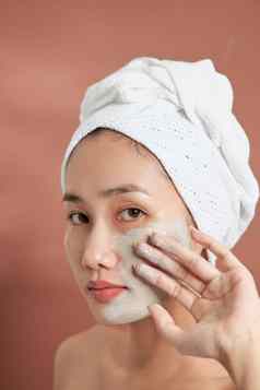 水疗中心亚洲女孩应用面部粘土面具美治疗蓝色的背景
