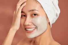 水疗中心亚洲女孩应用面部粘土面具美治疗蓝色的背景