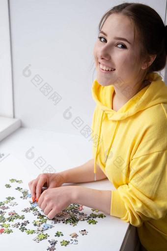 漂亮的浅黑肤色的女人女孩黄色的连帽衫安排块拼图谜题游戏明亮的白色房间玩董事会游戏首页