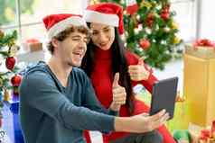 夫妇男人。女人显示拇指在线闲谈，聊天平板电脑圣诞节节日庆祝人正常的生活方式