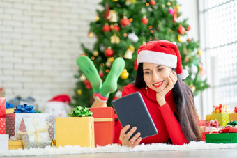 美丽的女人休息手持有平板电脑保持房间圣诞节树快乐在线购物首页圣诞节节日