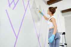 年轻的女人绘画山点缀墙油漆辊站梯