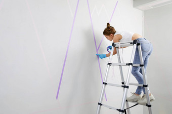 年轻的女人准备<strong>墙绘</strong>画站梯应用屏蔽磁带墙Diy项目