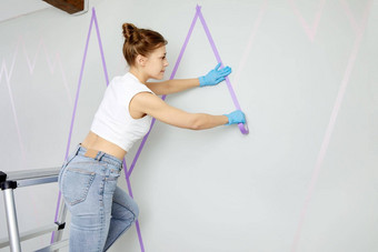 年轻的女人准备墙绘画站梯应用屏蔽磁带墙Diy项目