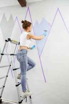 完整的长度视图年轻的女人绘画墙油漆辊屏蔽磁带站梯