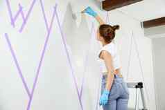 年轻的女人绘画山墙油漆辊屏蔽磁带站梯