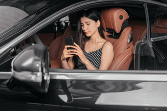 年轻的有吸引力的亚洲女人电话坐着奢侈品车前面海