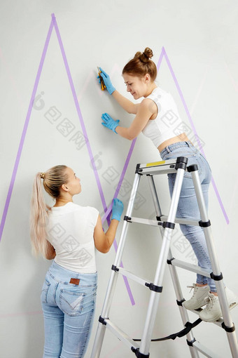 年轻的女人准备墙绘画站梯应用屏蔽磁带墙Diy项目