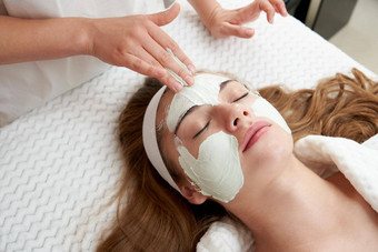 美容师应用振兴面部面具女脸美沙龙面部治疗概念