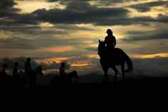 占主导地位的轮廓女人骑马骑集团开放地面山天空日落