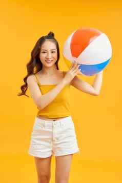 快乐年轻的亚洲女人持有海滩球夏天假期旅行橙色背景