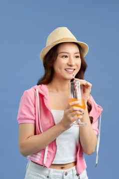 有吸引力的年轻的亚洲女人喝水果汁蓝色的背景