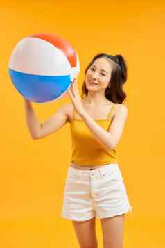 年轻的美丽的女人玩海滩球夏季橙色背景