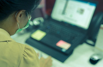 回来视图女人穿脸面具工作桌子上移动PC办公室亚洲女人工人电脑办公室工作首页正常的生活方式办公室冠状病毒流感大流行