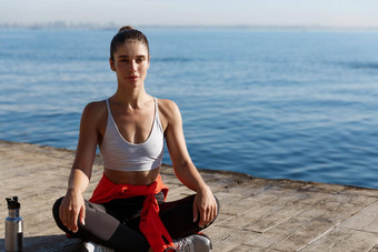 户外拍摄放松年轻的女人冥想海实践瑜伽坐着体式木码头地板上