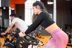 美丽的女人骑自行车现代健身自行车集团旋转类健身房