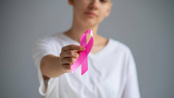 不知名的女人穿白色t恤持有粉红色的丝带象征乳房癌症白色背景