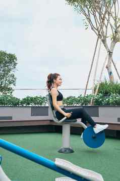 亚洲女人锻炼在户外健身房操场上设备