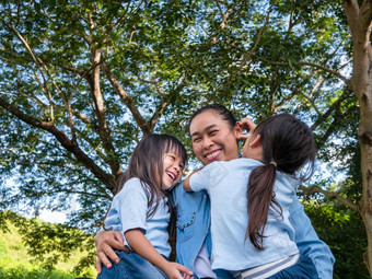 兄弟姐妹女孩妈妈笑拥抱温暖的阳光明媚的夏天一天花园年轻的女孩妈妈。支出一天公园