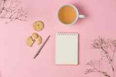 平躺笔记本粉红色的背景茶饼干