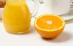 一半成熟的橙色新鲜挤压汁玻璃透明的玻璃水瓶白色表格