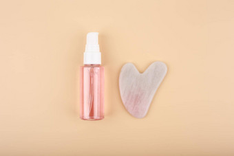 按摩过来这里血清石油透明的瓶心形状的刮痧疗法粉红色的石英水晶米色背景