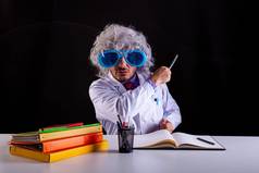 疯狂的科学老师白色外套不整洁的头发有趣的眼睛眼镜坐着桌子上