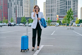 中间岁的业务女人手提箱会说话的移动电话户外停车