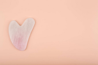 粉红色的心形状的<strong>刮痧</strong>疗法石头使石英水晶明亮的米色背景
