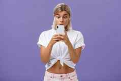 女孩看激动人心的视频社会媒体无线耳机持有智能手机脸出现眼睛智能手机屏幕盯着小工具感兴趣好奇心紫色的背景