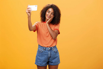 女人使化妆一天帖子照片在线采取自拍品牌智能手机使可爱的脸倾斜头棕榈微笑轻轻设备屏幕摆姿势橙色背景