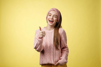 快乐逗乐美丽的年轻的欧洲女孩毛衣针织头巾显示好手势满意服务提供眨眼时髦的微笑翘拇指批准给建议