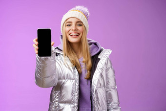 时髦的很高兴快乐的金发碧眼的女人推荐应用程序编辑完美的<strong>图片</strong>持有智能手机显示移动电话显示自豪地令人满意的微笑相机站<strong>紫色</strong>的背景
